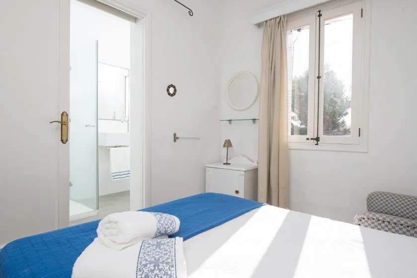Un dormitorio luminoso con una cama, una puerta abierta al baño y una ventana.
