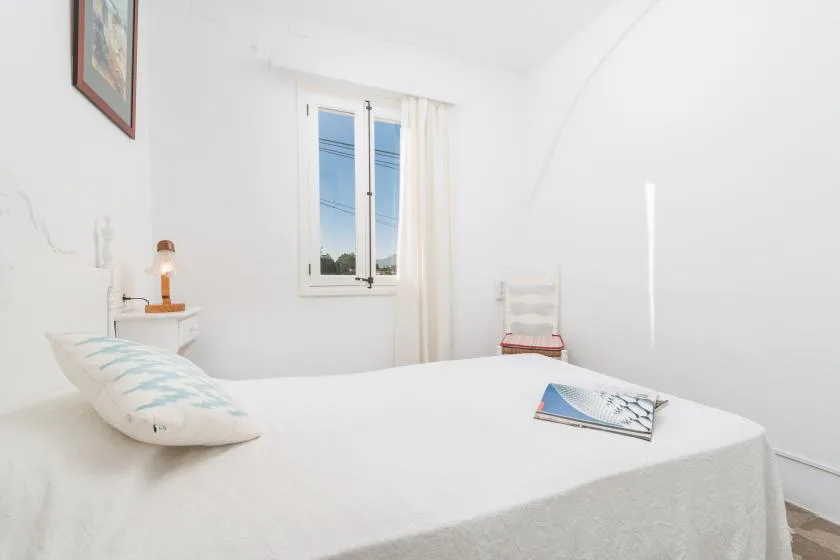 Un dormitorio luminoso con una cama blanca junto a una ventana.