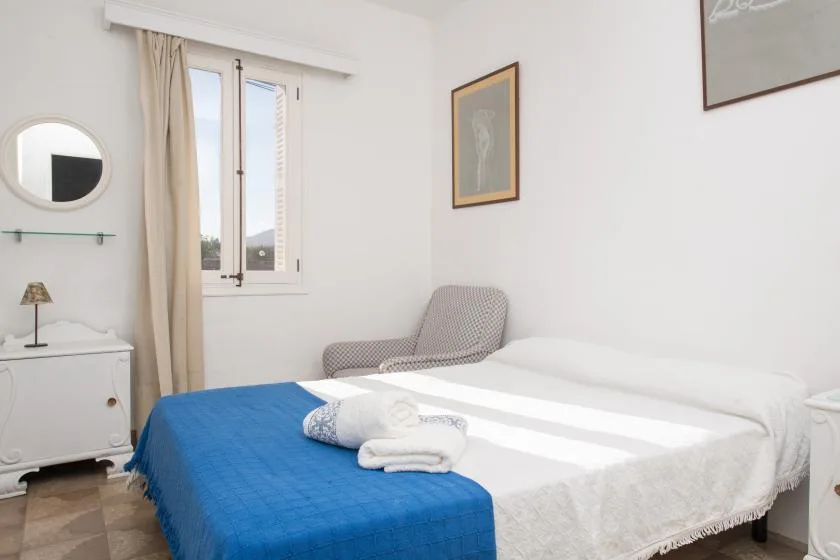 Un dormitorio luminoso con una cama cubierta de ropa blanca y una manta azul.