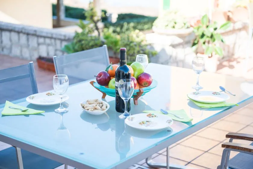 Una mesa de comedor al aire libre está puesta con platos, copas y un frutero.