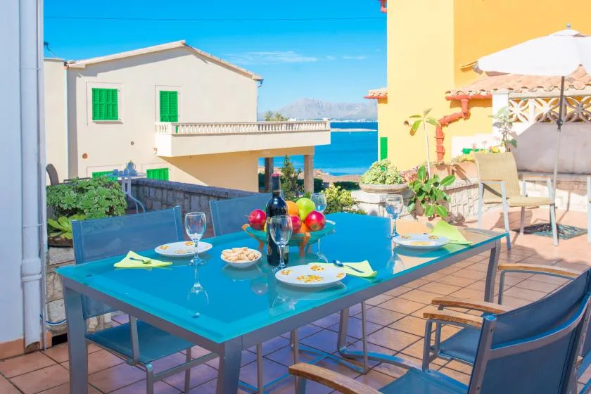 Una zona de comedor en una terraza junto al mar, con mesa de cristal y adornos coloridos.