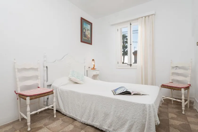 Un dormitorio con una cama cubierta de ropa de cama blanca y dos sillas.