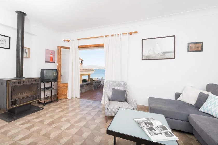 Una sala luminosa con asientos, una mesa de centro y una puerta abierta a un balcón.