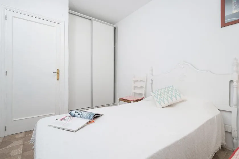 Un dormitorio luminoso con una cama blanca y puertas corredizas de armario.