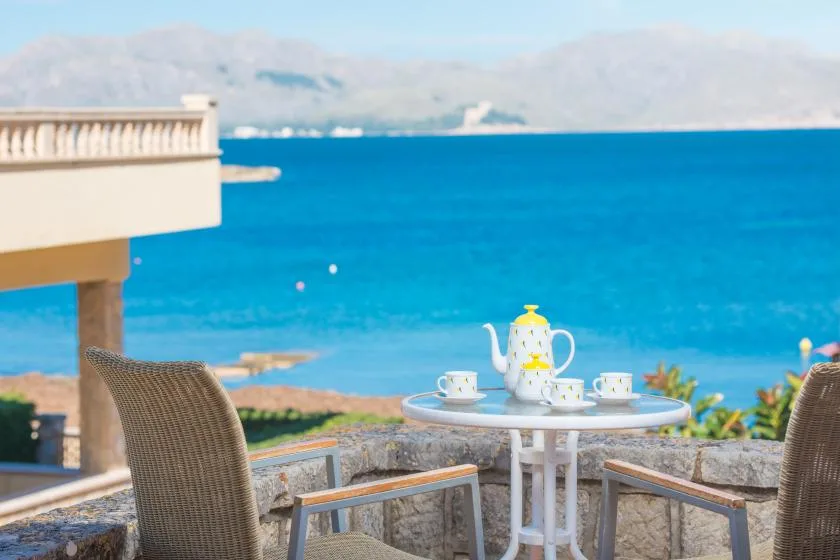 Un patio junto al mar, con una mesa redonda y asientos, da a aguas azules.