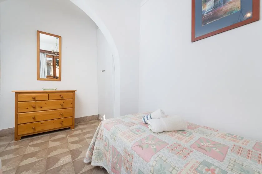 Un dormitorio con una colcha estampada, una cómoda de madera y un espejo de pared.