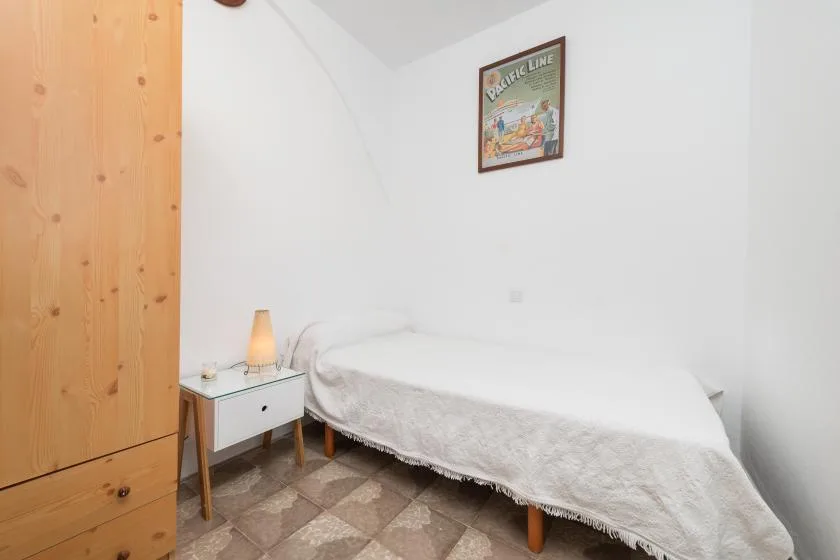 Un dormitorio con una cama individual, una mesita de noche y un armario de madera.