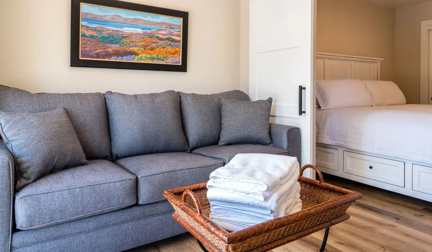 Una zona de estar en un dormitorio, con un sofá gris y ropa doblada sobre una mesa.