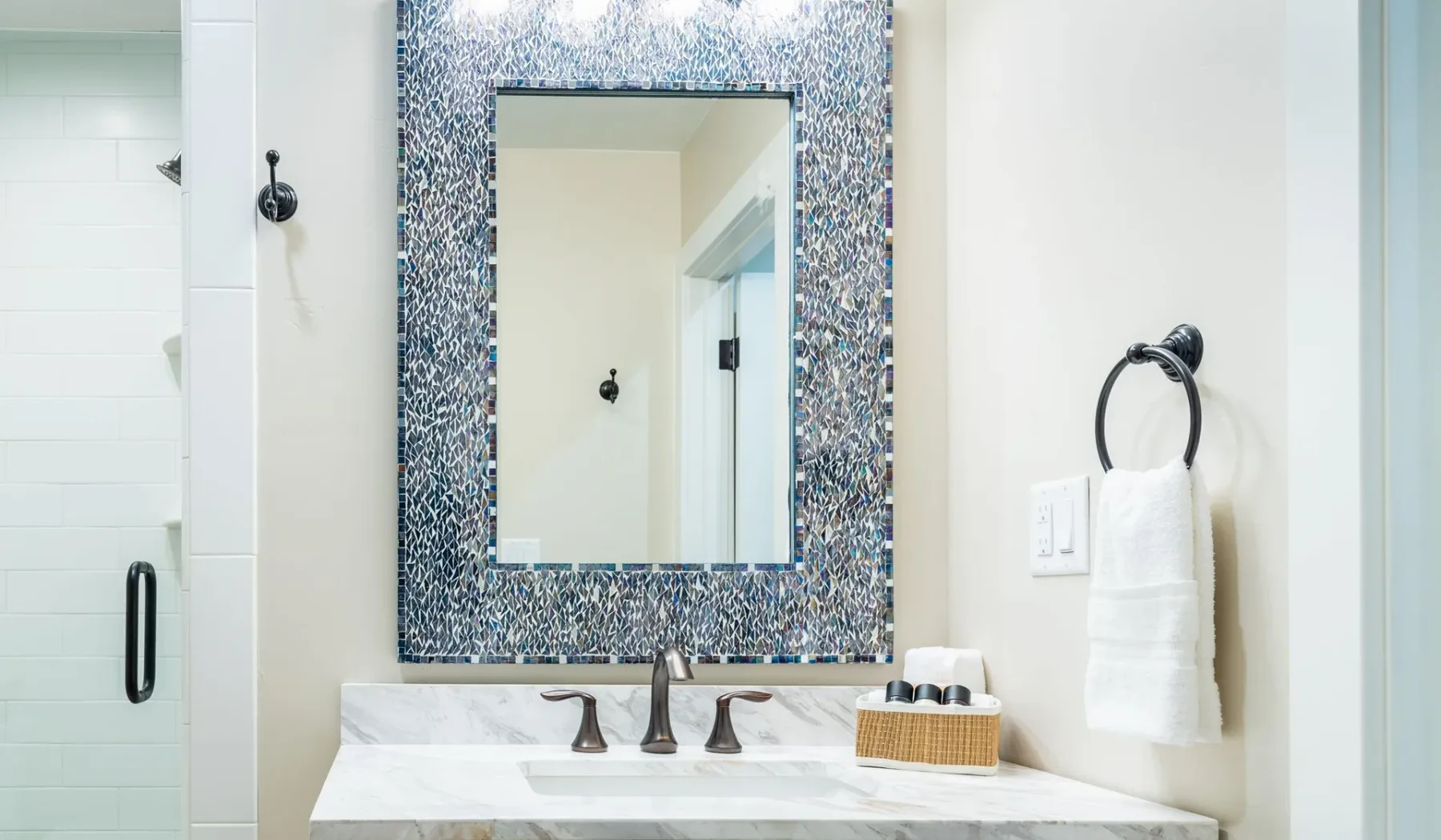 Un lavabo de baño con un gran espejo enmarcado en mosaico y una toalla en la pared.