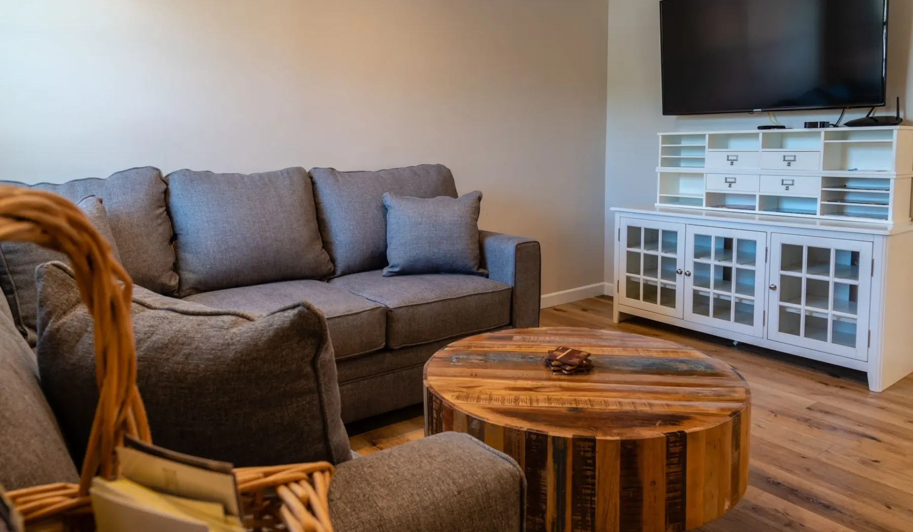 Una sala de estar con asientos grises, una mesa de centro de madera y un televisor.