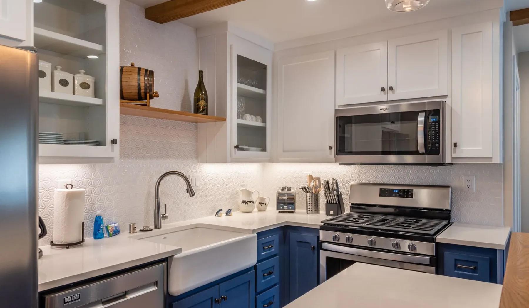 Una cocina luminosa con gabinetes superiores blancos, gabinetes inferiores azules y electrodomésticos de acero inoxidable.