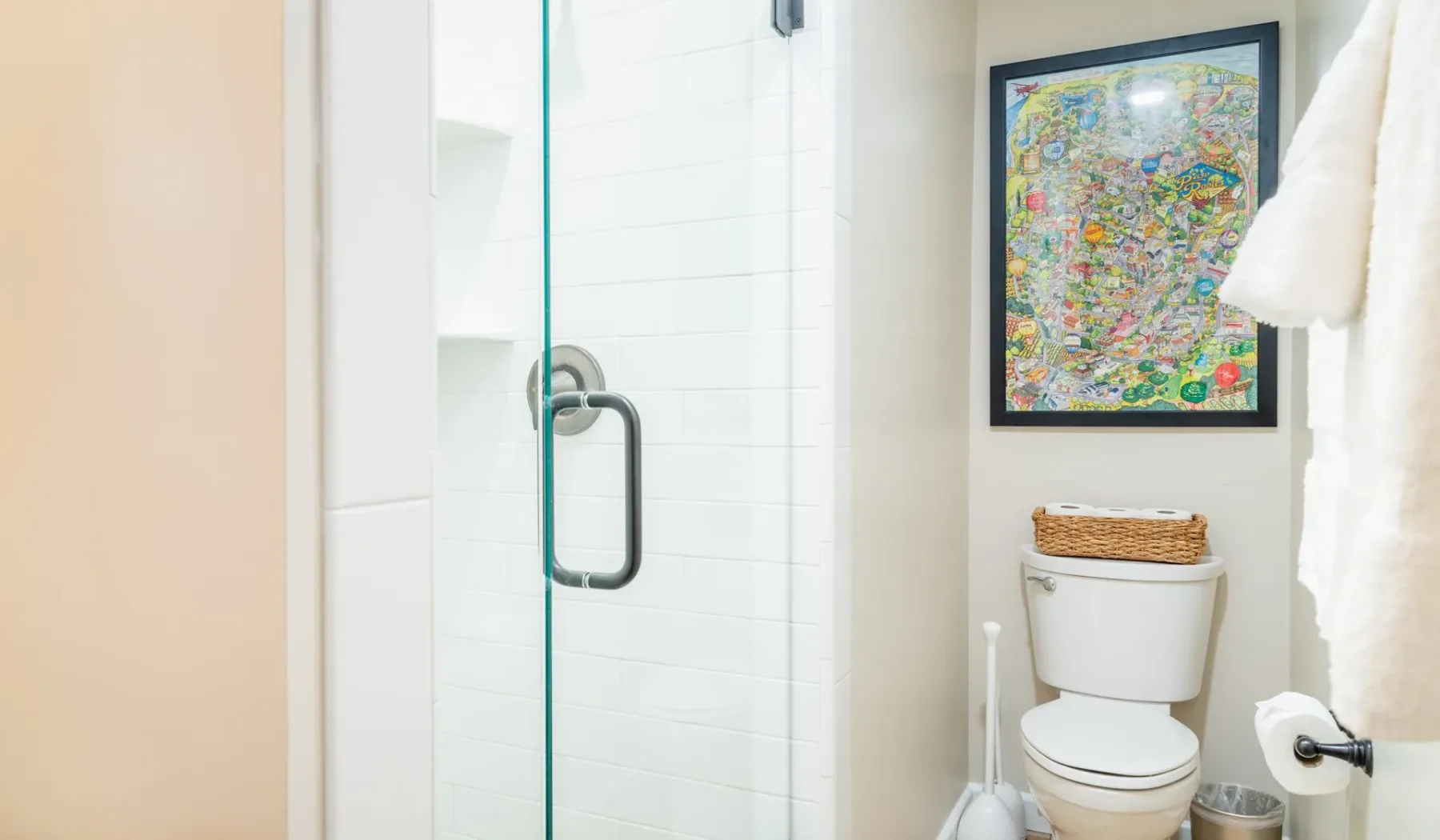 Un baño luminoso con ducha de vidrio, inodoro y una obra enmarcada.