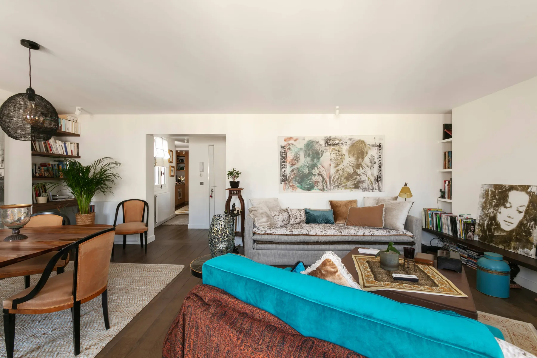A bright living room with a sofa, colorful artwork, and a turquoise seating piece.