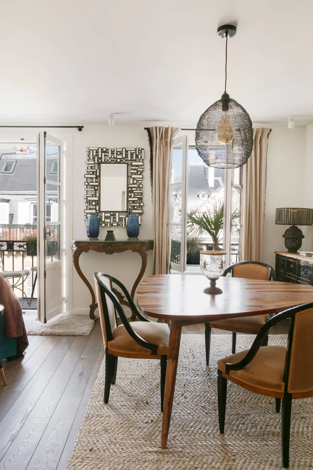 A dining area with a round wooden table, chairs, and large windows.