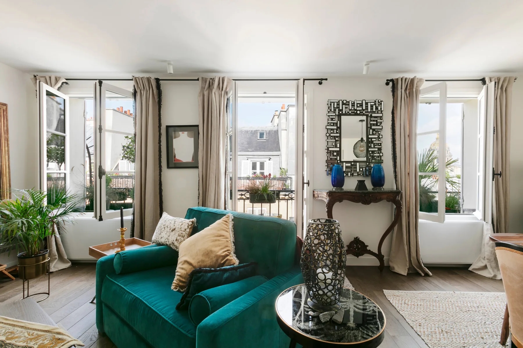 A bright living room with teal seating, tall windows, and a decorative mirror.