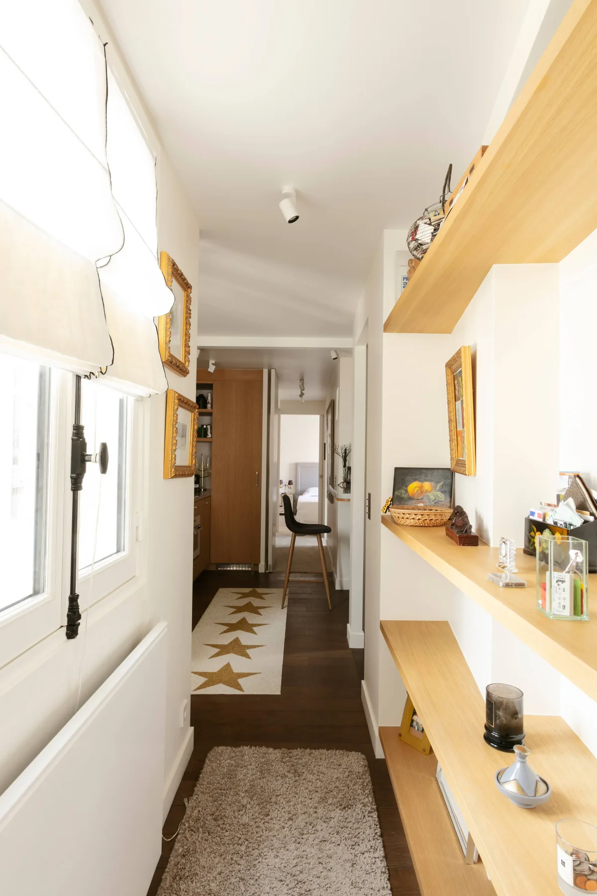 A narrow hallway with windows on one side and long wooden shelves on the other.