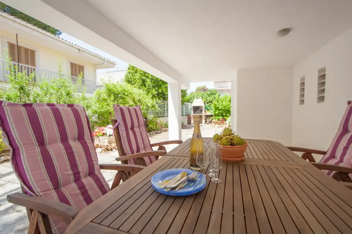 A covered outdoor dining area with a wooden table and striped seating.