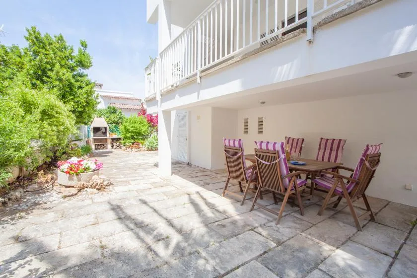 Un patio exterior embaldosado con una mesa y asientos bajo un balcón blanco.