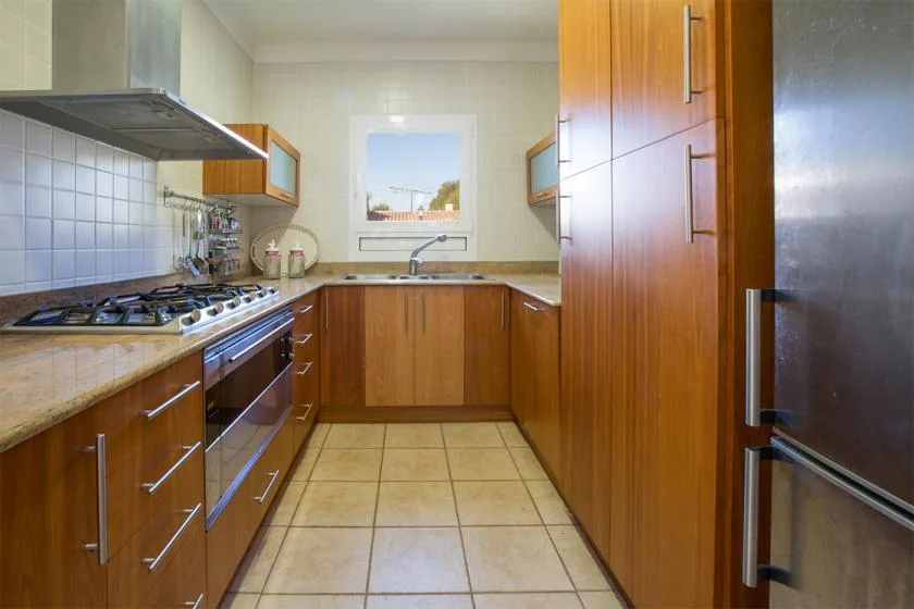 A galley kitchen with wooden cabinets, tiled counters, and a gas cooktop.