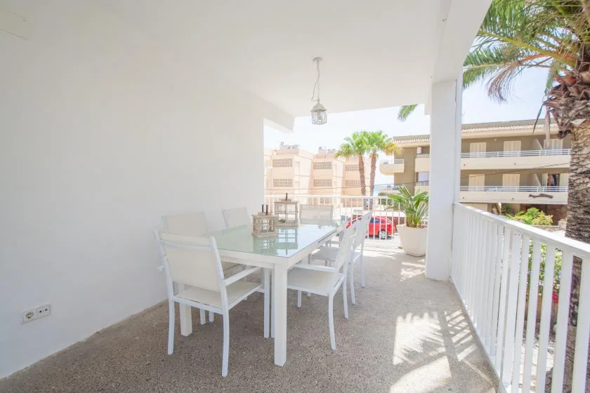 Un balcón cubierto tiene una mesa blanca y asientos con vista a edificios cercanos.