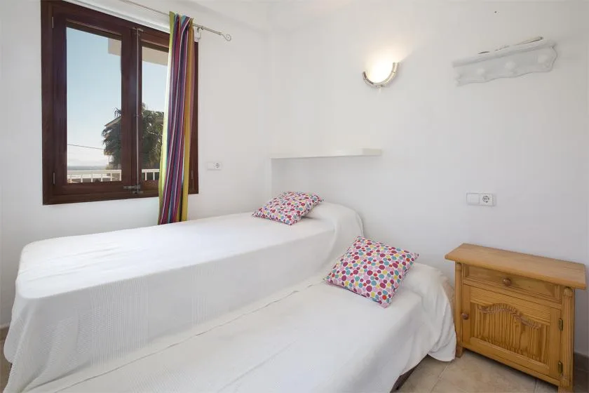 A bright bedroom with two single beds and a wooden bedside cabinet.
