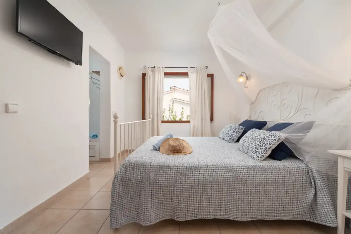 A bedroom with a double bed beneath a white canopy and a window.