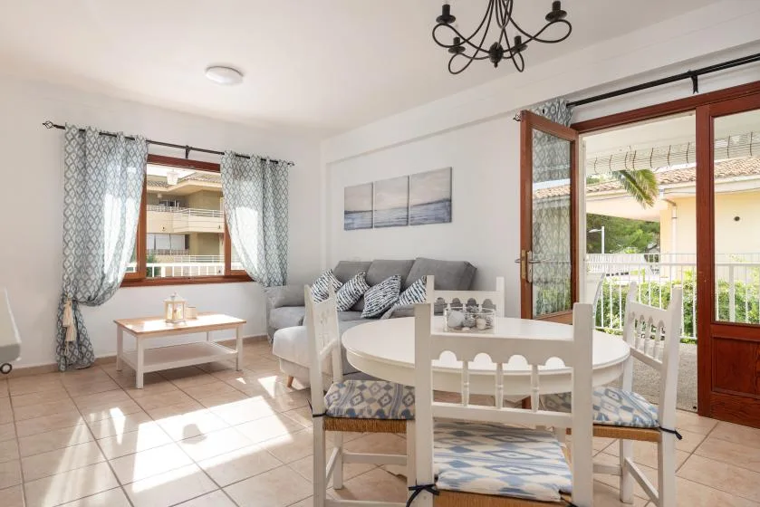 A bright living and dining area with seating beside an open balcony door.