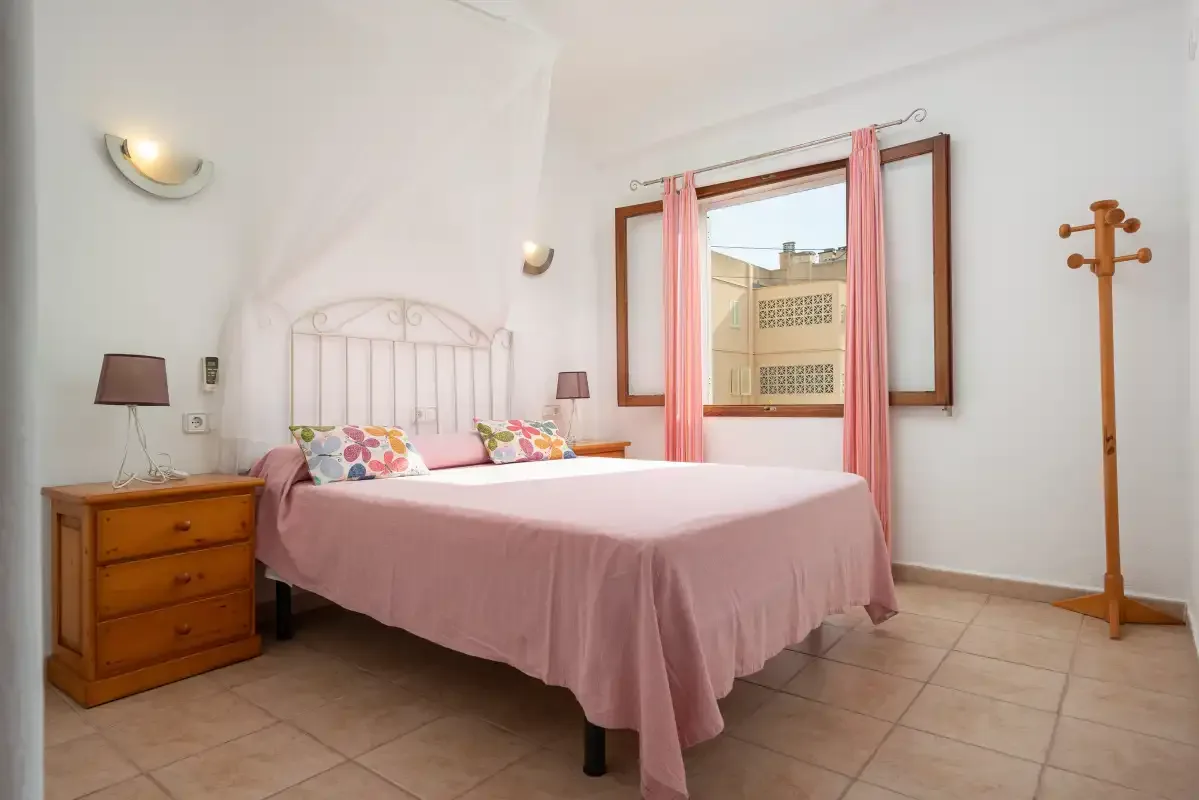 A bedroom with a pink bedspread, bedside furniture, and a window.