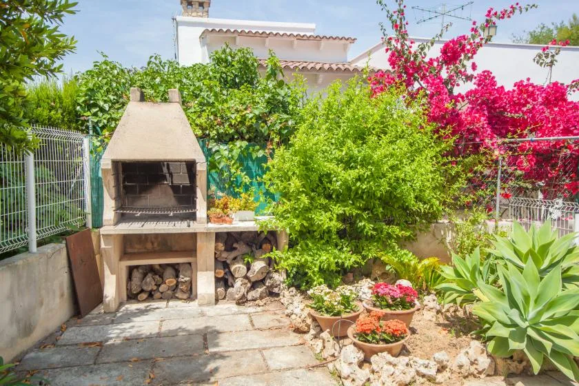 A garden patio features a built-in grill, flowering plants, and leafy greenery.