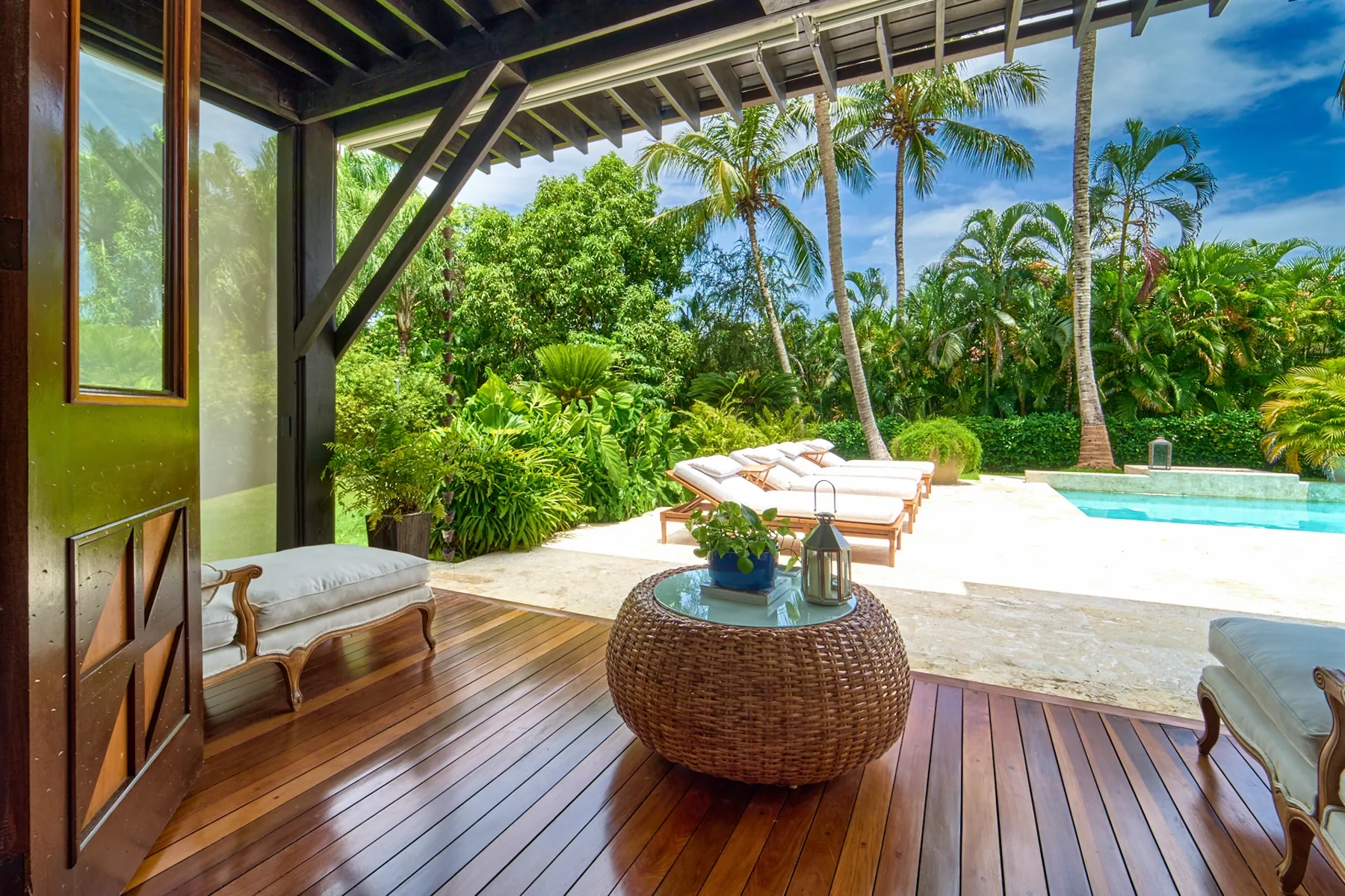 A covered outdoor seating area overlooks a swimming pool and tropical garden.
