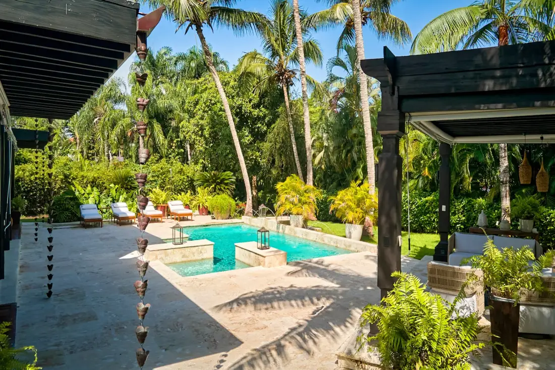 An outdoor pool sits among tropical plants and palm trees.