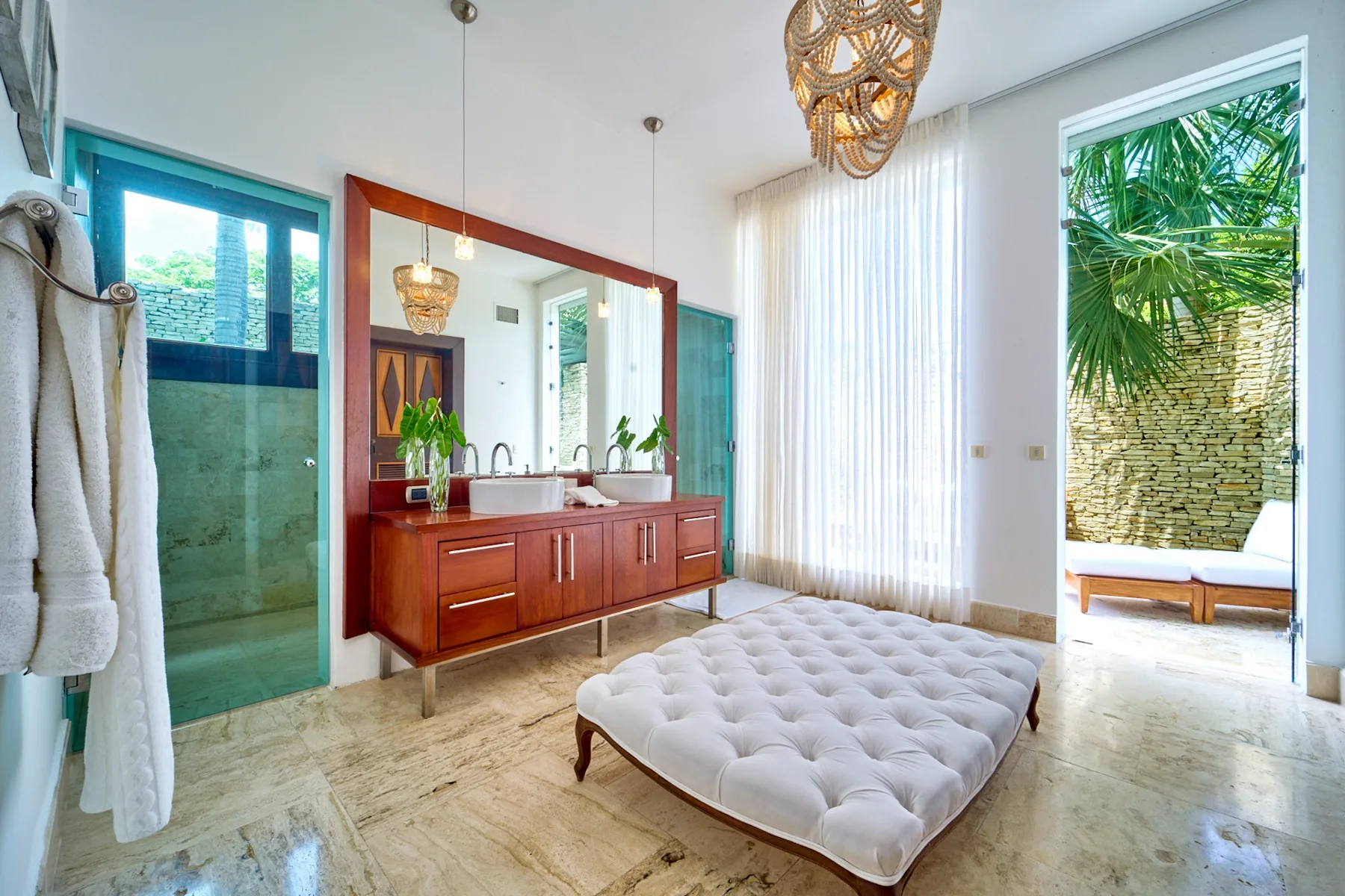 A bright bedroom with a low bed beside a vanity and large windows.