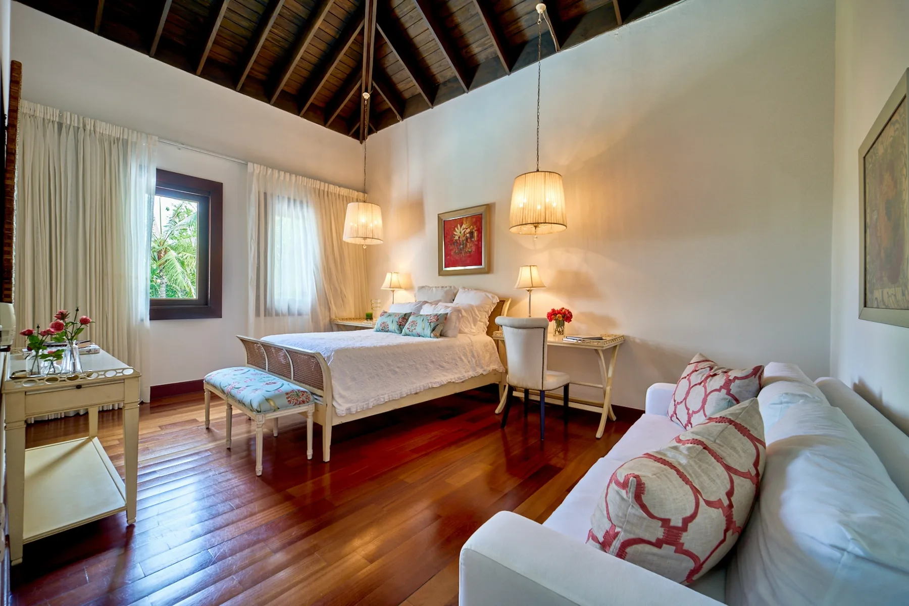 A bedroom with a bed, seating area, and exposed wooden ceiling.