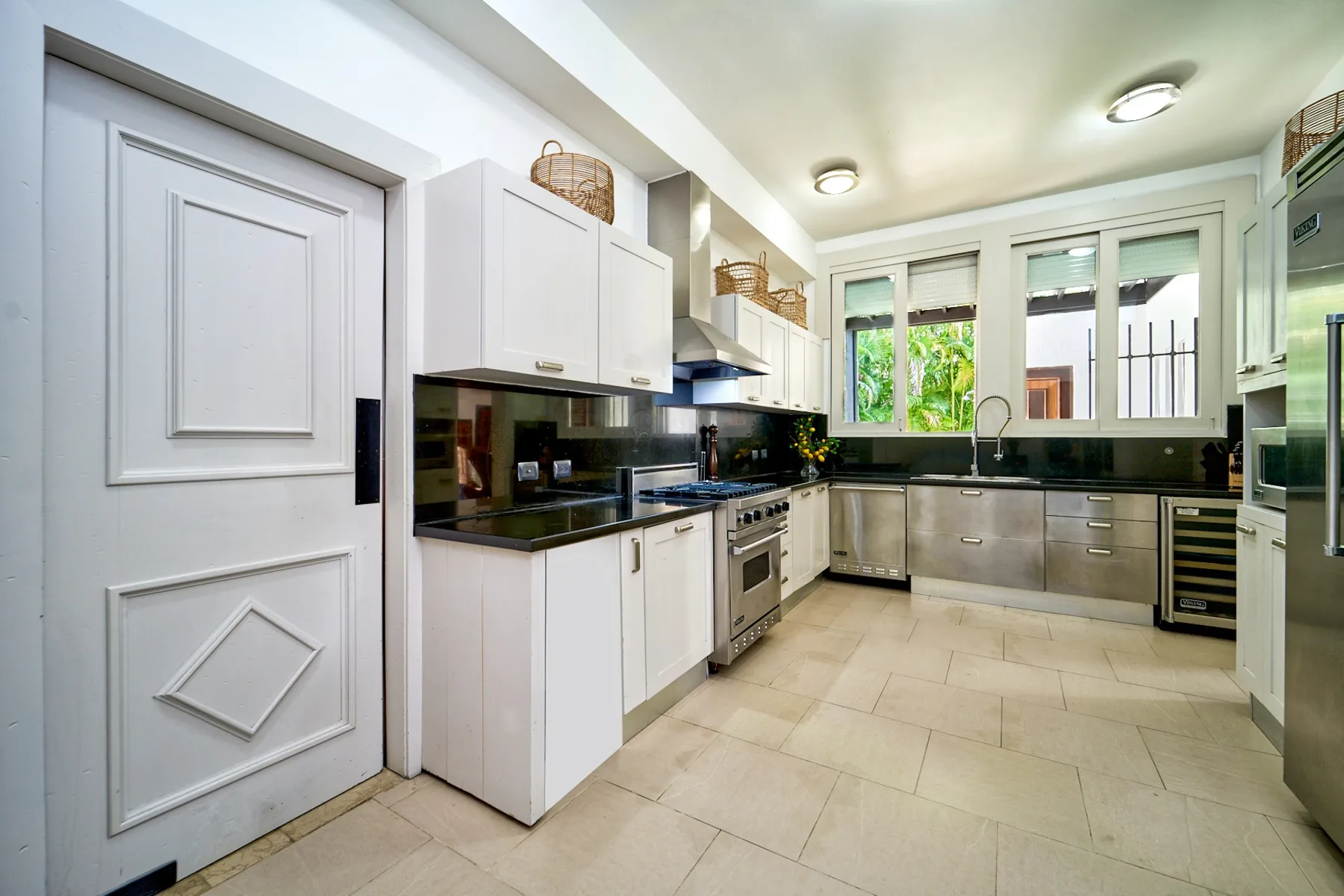 A bright kitchen with dark countertops, light cabinets, and windows overlooking greenery.