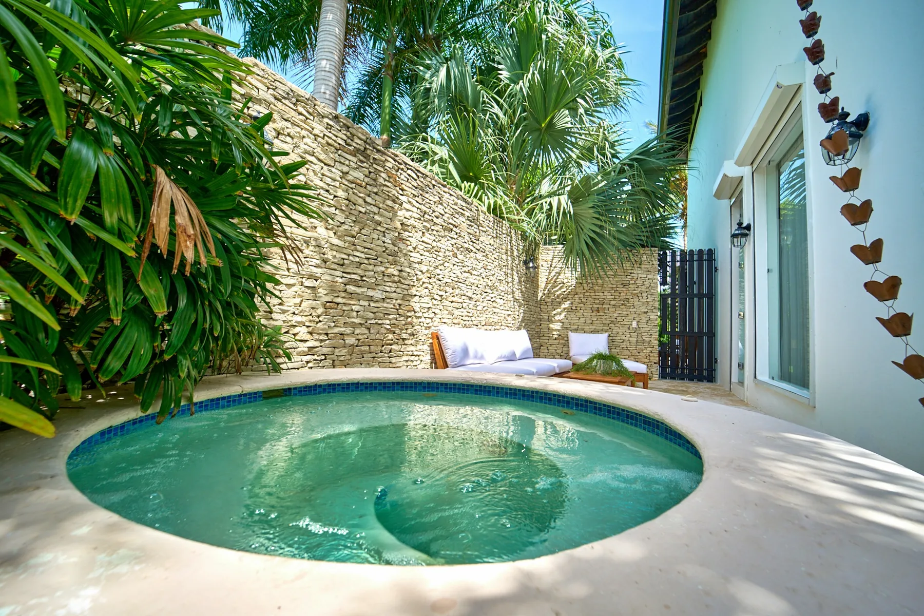 A small outdoor pool sits beside a pale building and a stone wall.