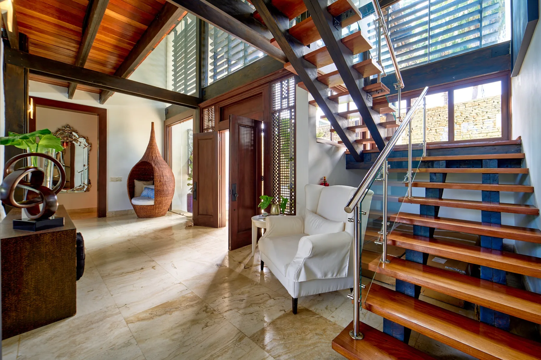 A bright interior with a staircase, a white armchair, and a sculptural fireplace.