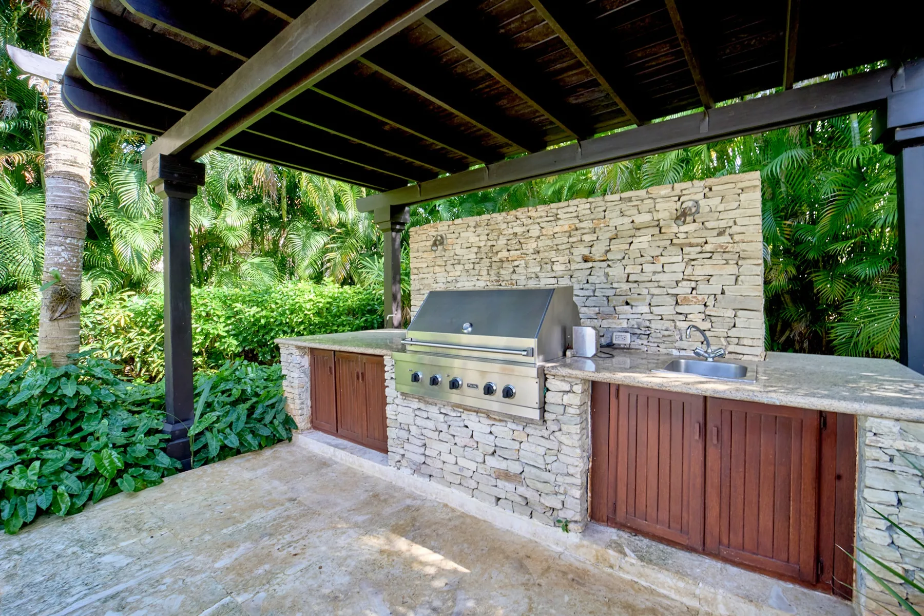 A covered outdoor kitchen with a built-in grill and stone counter.