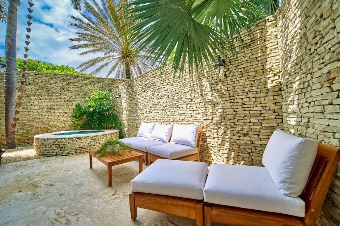An outdoor patio with cushioned seating, a wooden table, and a small pool.
