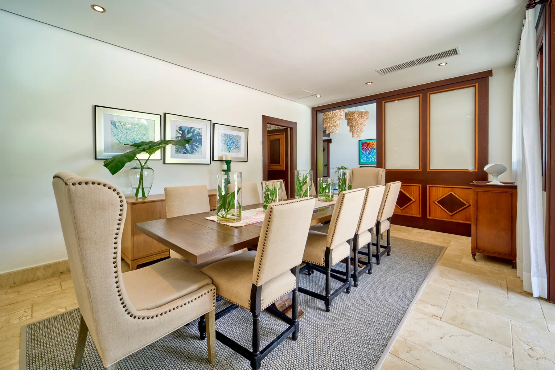 A dining room with a long table and upholstered seating on a rug.