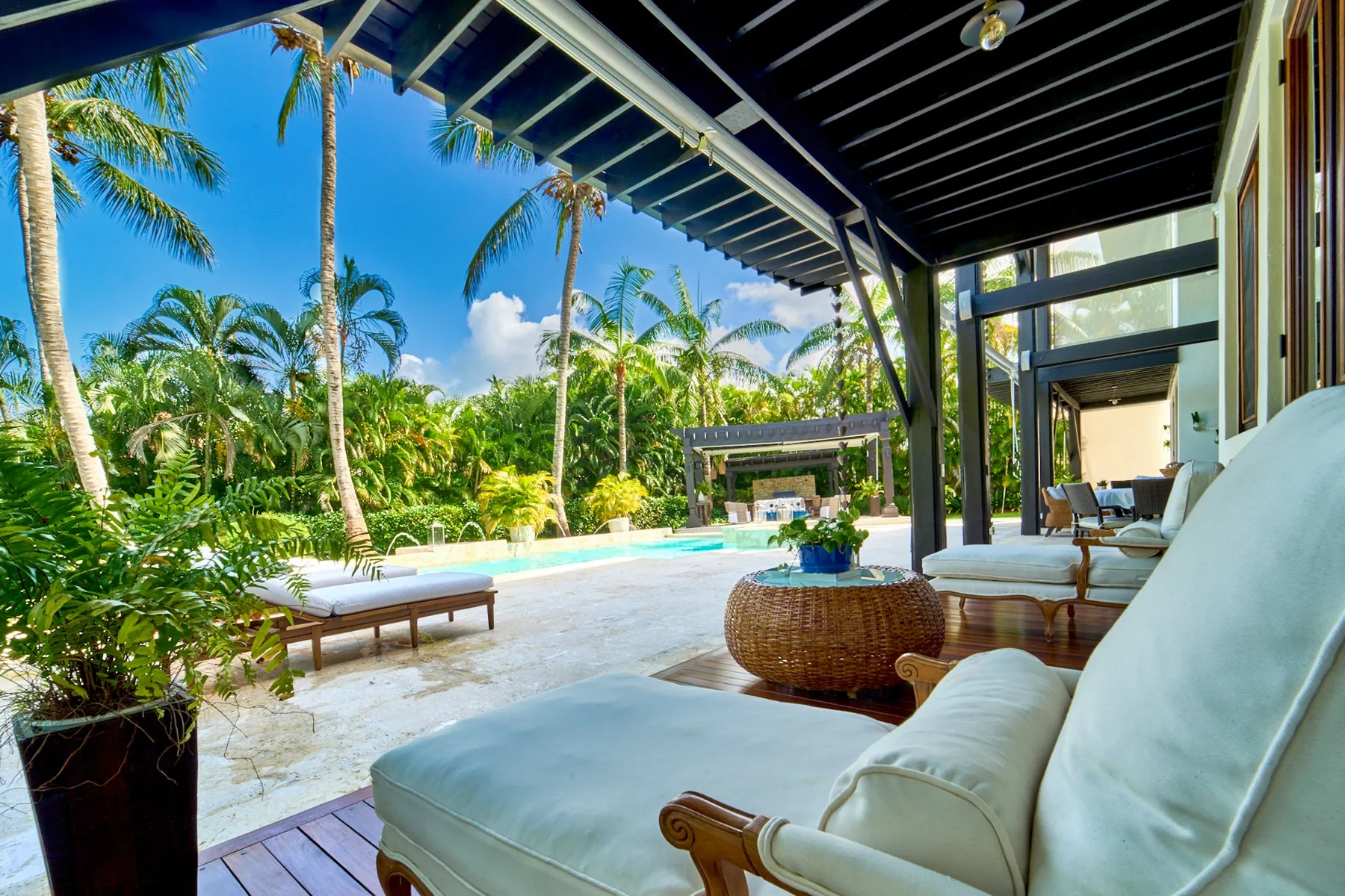 A covered patio seating area overlooks a swimming pool and tropical greenery.