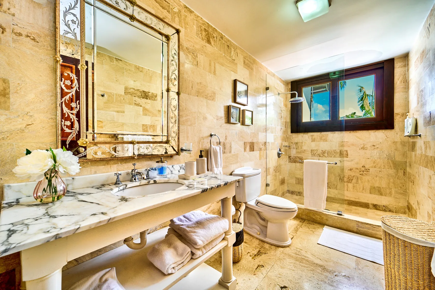 A tiled bathroom with a long sink counter, mirror, and window.