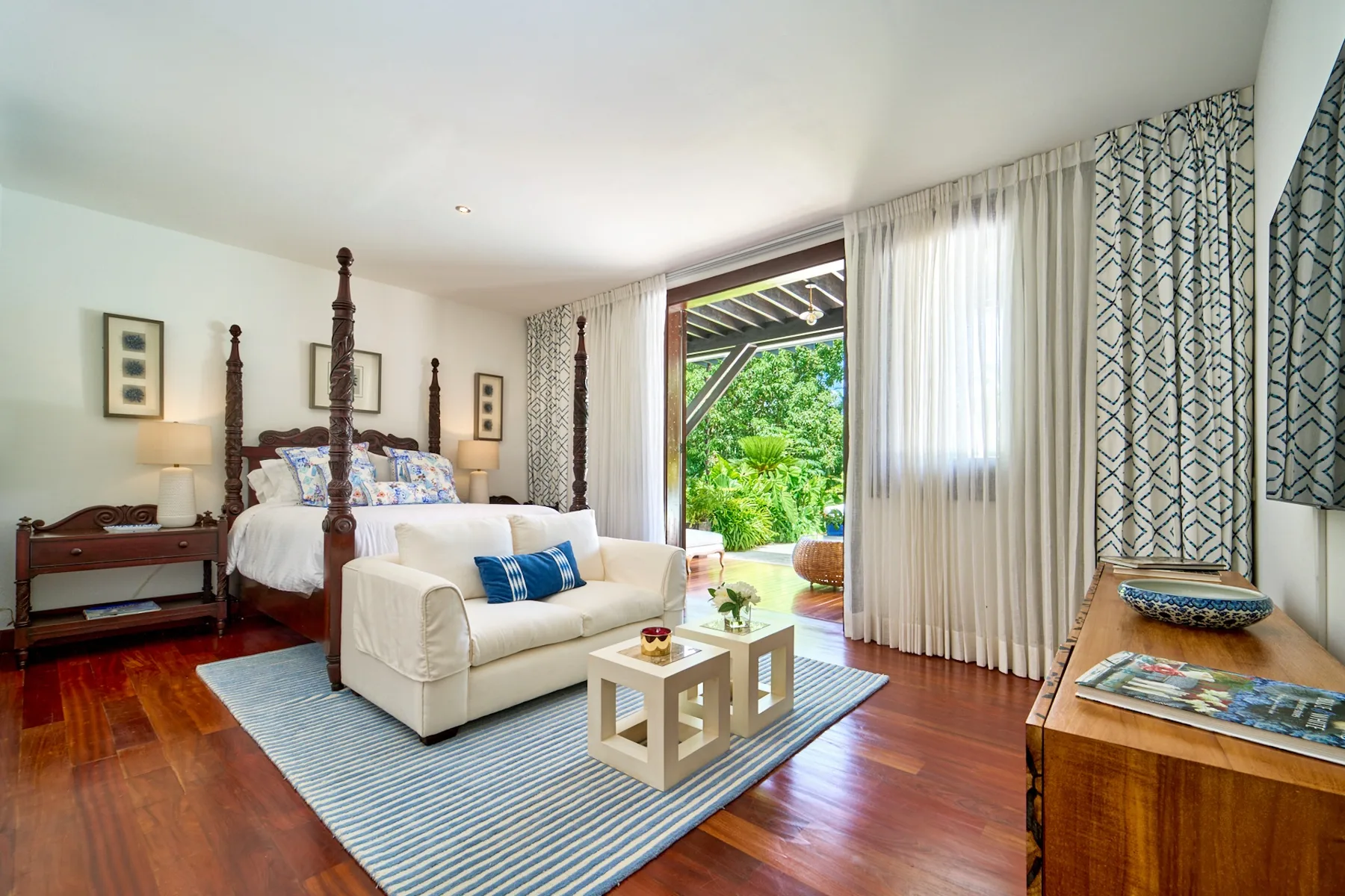 A bright bedroom with a white seating area beside an open doorway to greenery.