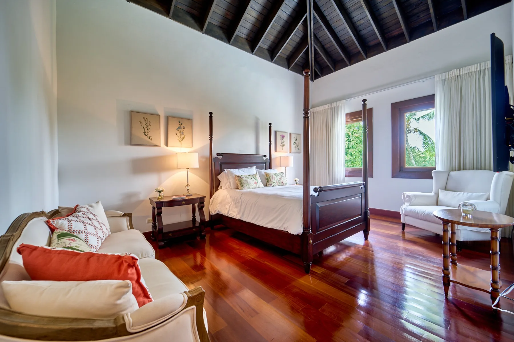A bright bedroom with a four-poster bed, seating, and tall windows.
