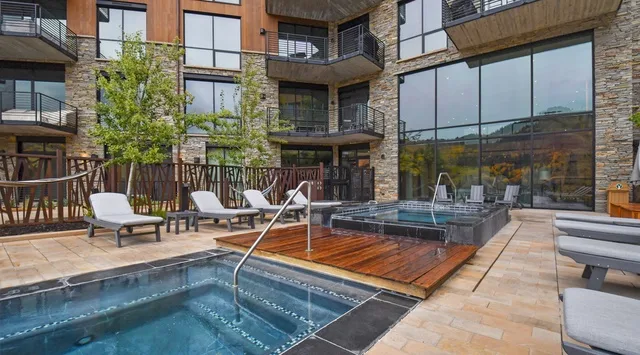 Una piscina exterior y una bañera de hidromasaje junto a un patio ajardinado.