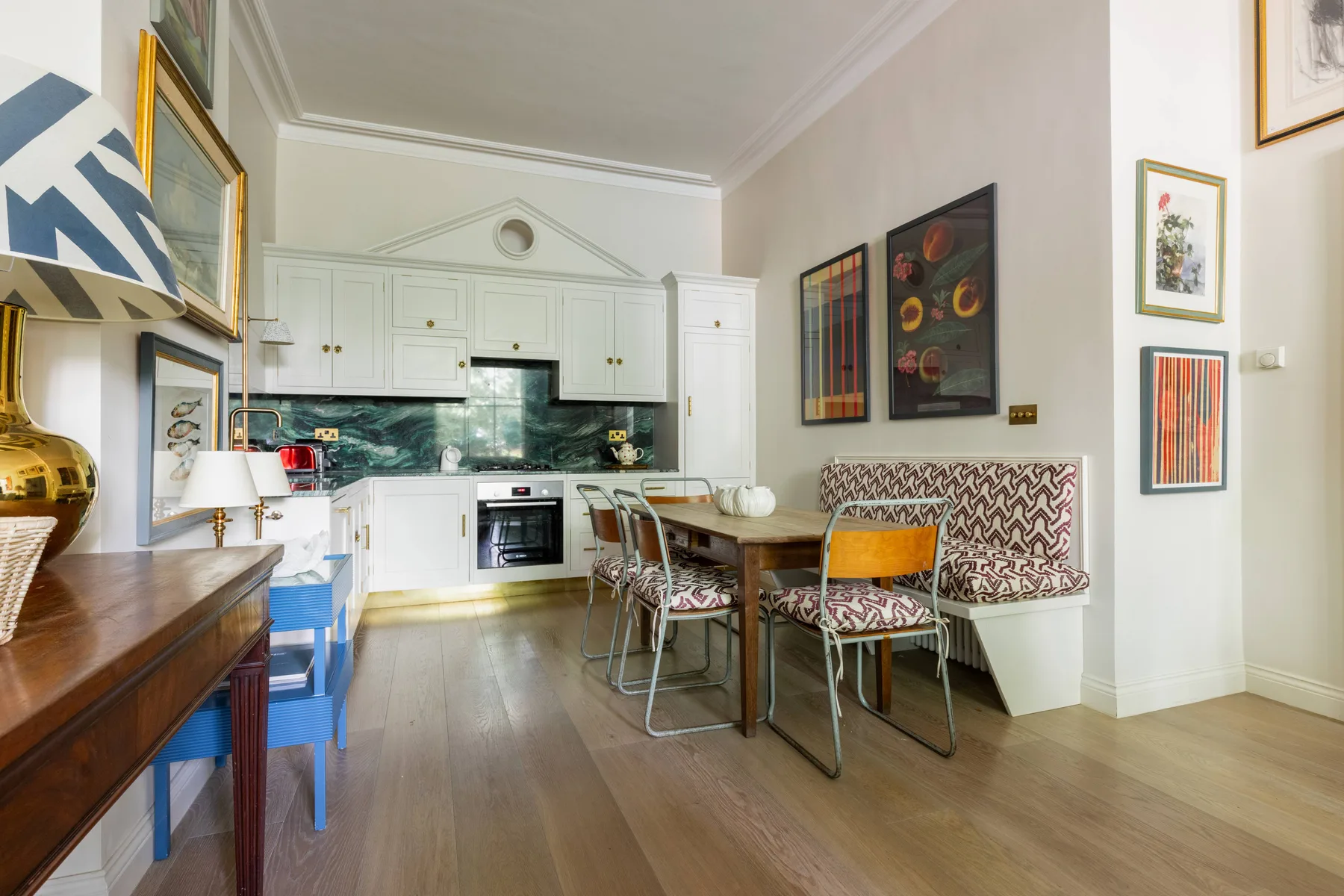 Una cocina y comedor luminosos, con armarios blancos y una mesa junto a asientos tapizados.