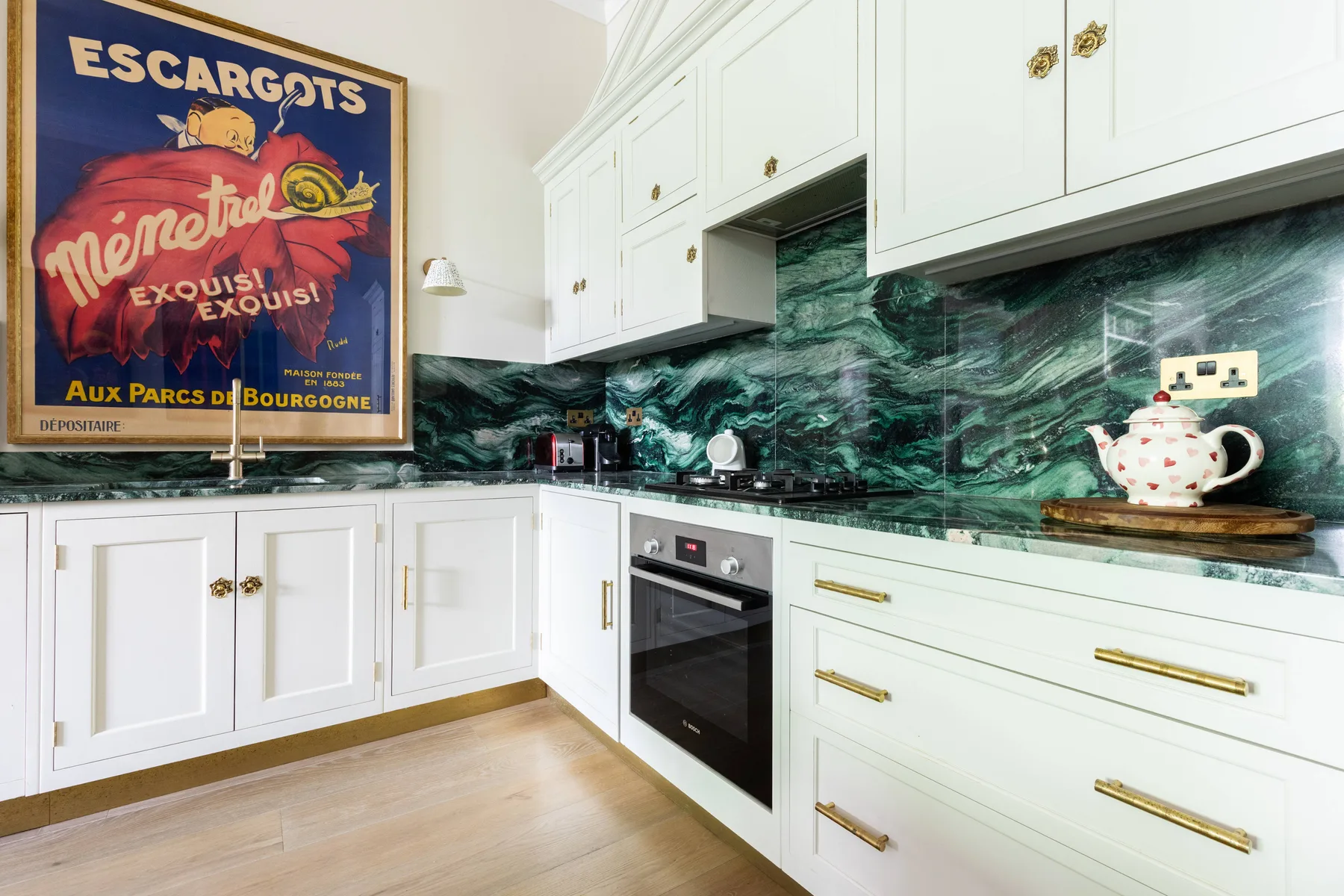 Una cocina luminosa con gabinetes blancos, un salpicadero verde oscuro y un horno integrado.
