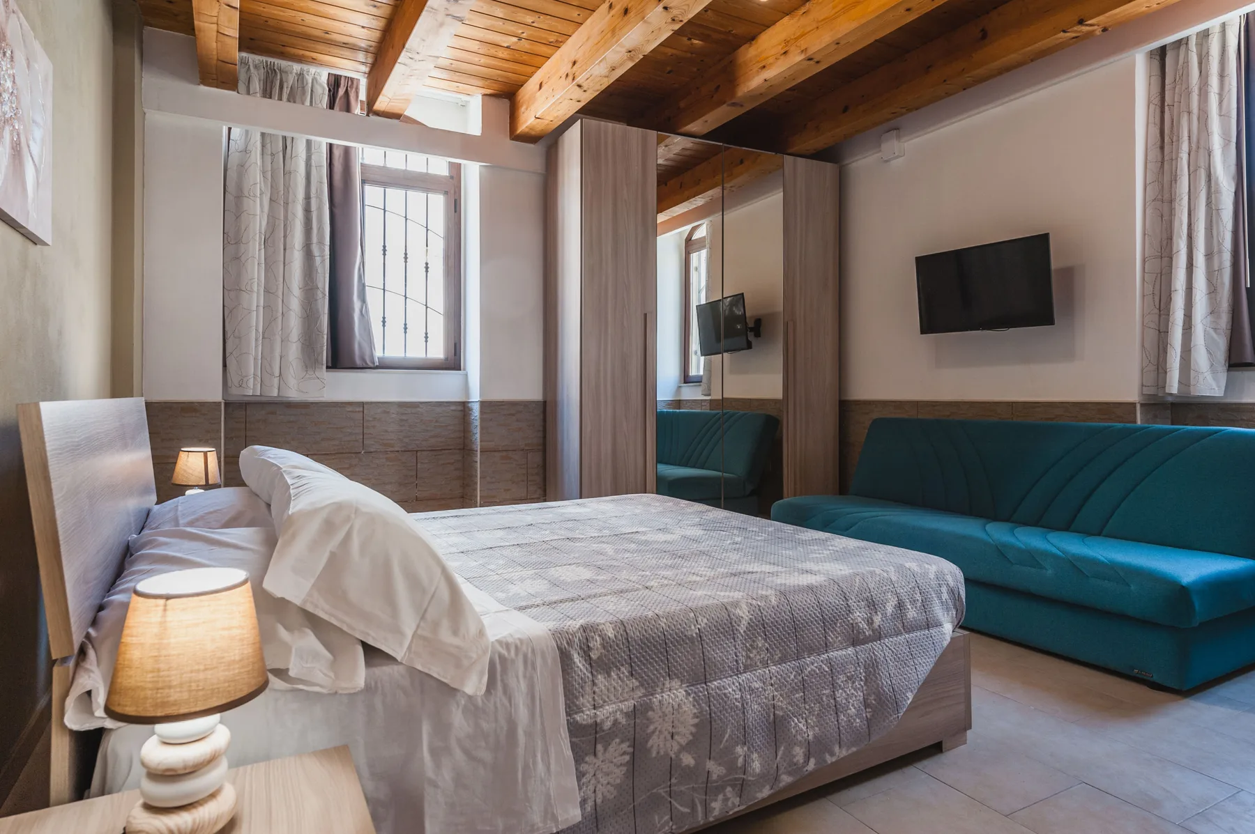 Un dormitorio con una cama, asientos verde azulado y vigas de madera a la vista.