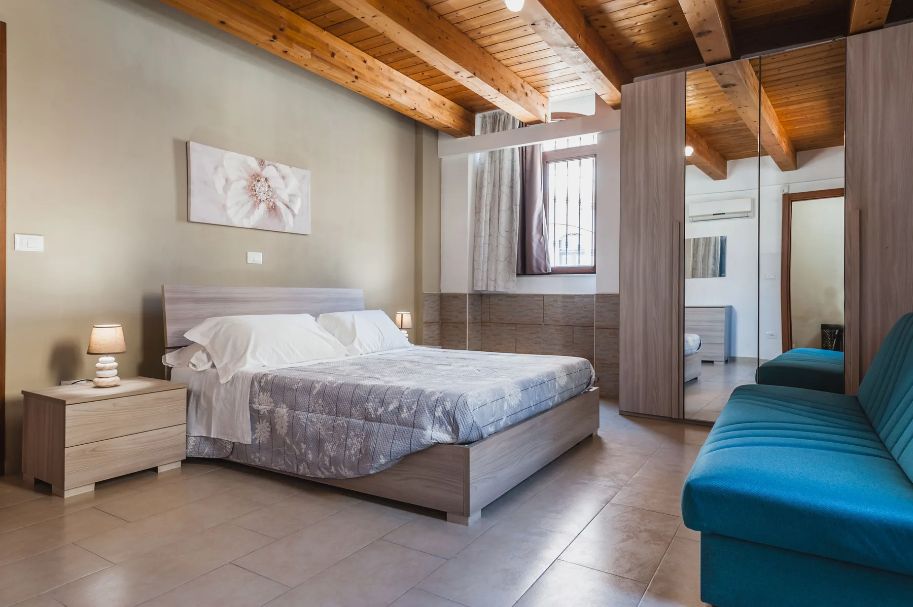 Un dormitorio con una cama, mesitas de noche y una zona de asientos tapizada en azul.