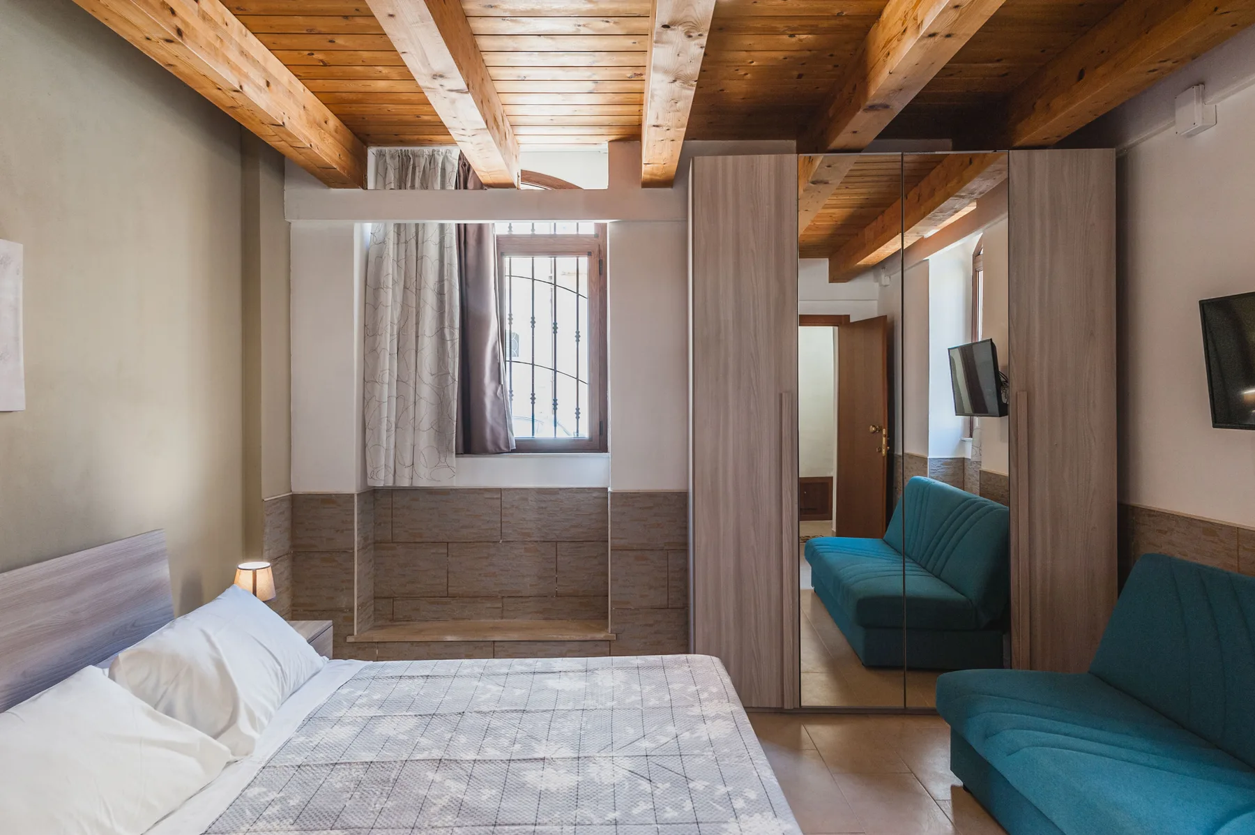 Un dormitorio con una cama y asientos color turquesa bajo un techo de madera expuesta.