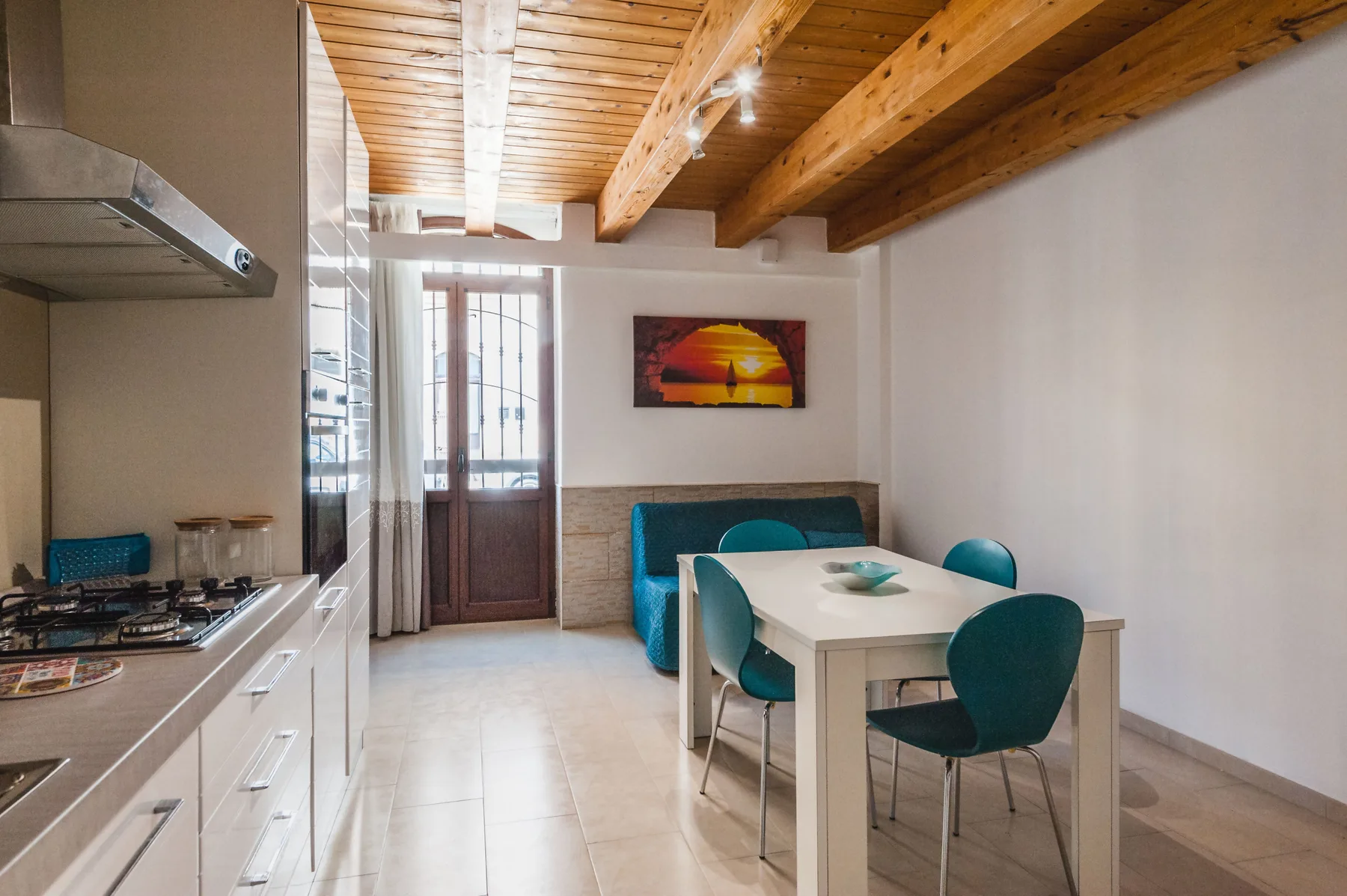 Una cocina y comedor con una mesa blanca y asientos color turquesa bajo un techo de madera.
